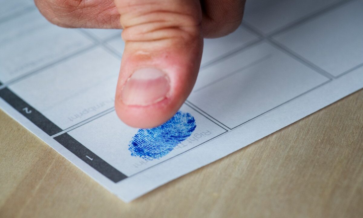 Kciuk przyciśnięty do karty daktyloskopijnej z polami na odciski, obok niebieski odcisk kciuka w polu oznaczonym jako prawy kciuk