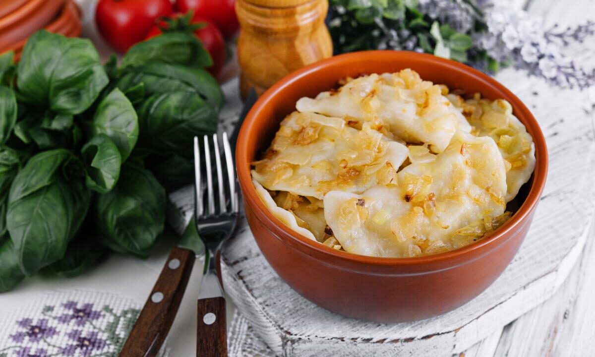 Pierogi z nadzieniem ziemniaczanym w glinianej misce na stole, obok świeże zioła i pomidory