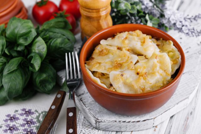 Pierogi z nadzieniem ziemniaczanym w glinianej misce na stole, obok świeże zioła i pomidory