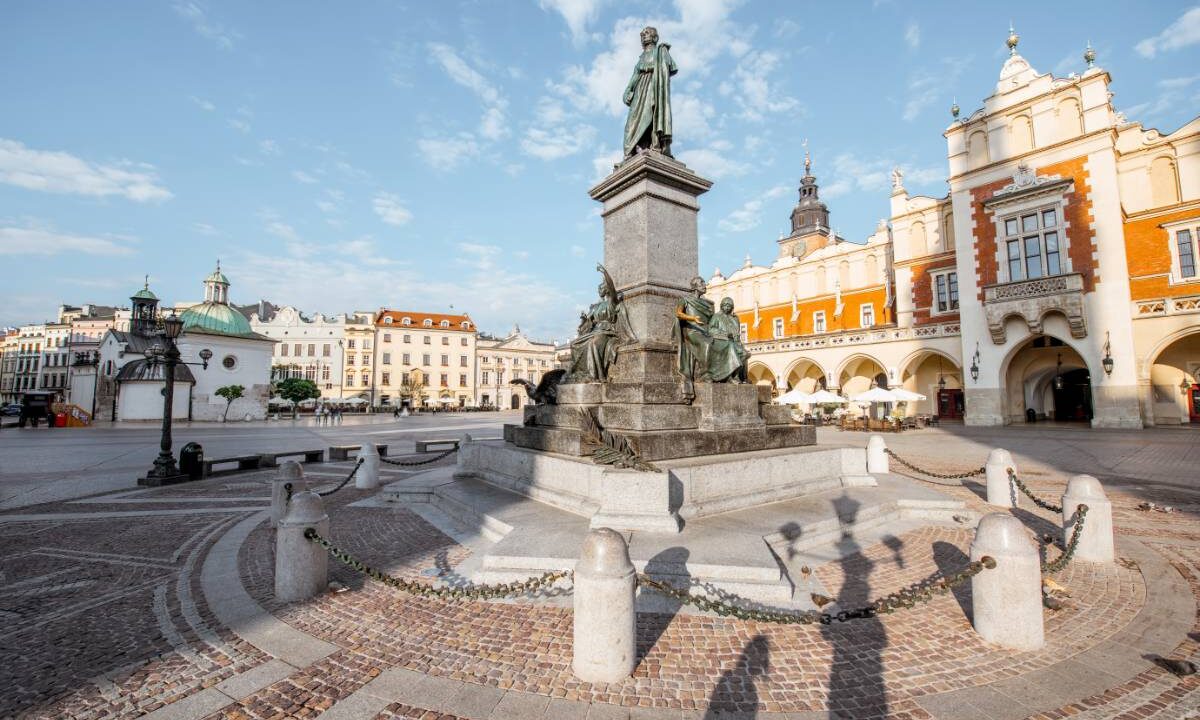 Pomnik Adama Mickiewicza na Rynku Głównym w Krakowie, w tle Sukiennice w porannym świetle