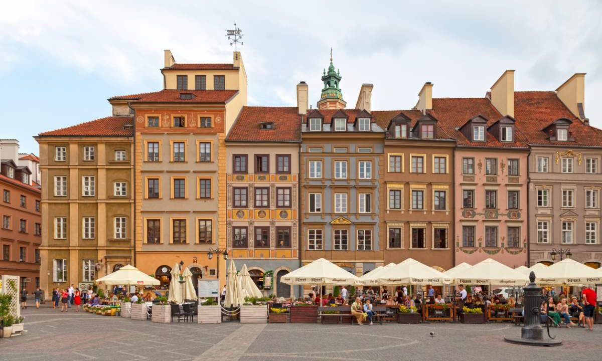 Kolorowe kamienice na Rynku Starego Miasta w Warszawie, przed nimi ogródki kawiarniane pod białymi parasolami