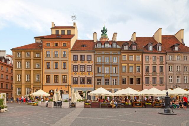 Kolorowe kamienice na Rynku Starego Miasta w Warszawie, przed nimi ogródki kawiarniane pod białymi parasolami