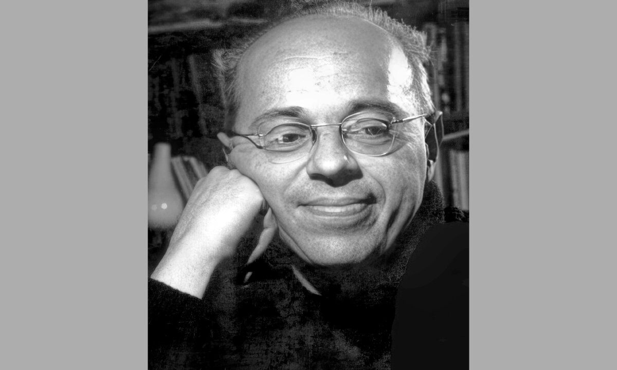 Stanisław Lem w okularach, z dłonią przy policzku, na tle regału z książkami, 1966 r.
