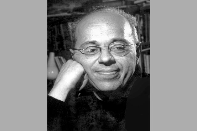 Stanisław Lem w okularach, z dłonią przy policzku, na tle regału z książkami, 1966 r.